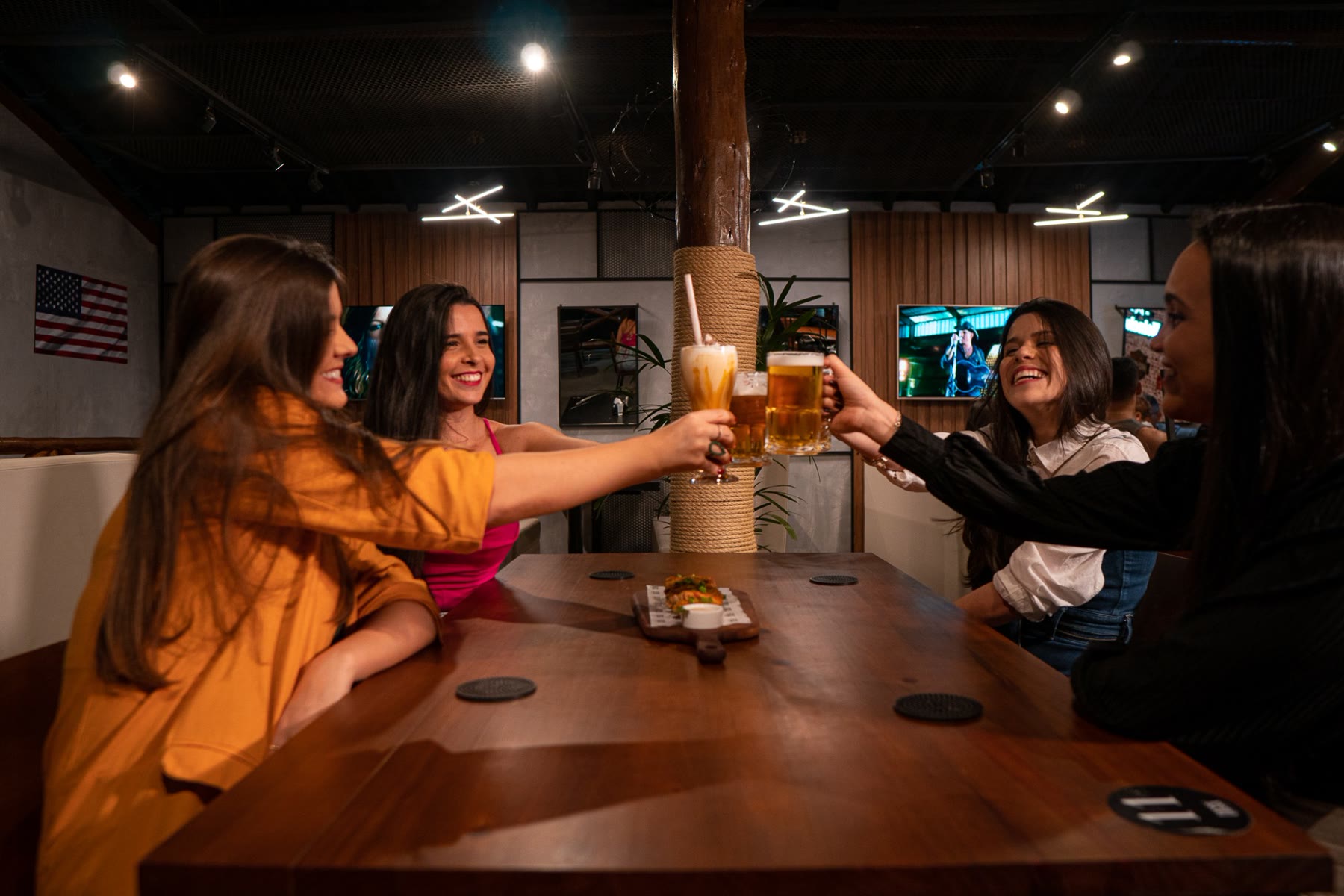 Quatro amigas brindando com chope e milkshake em uma mesa do Deck