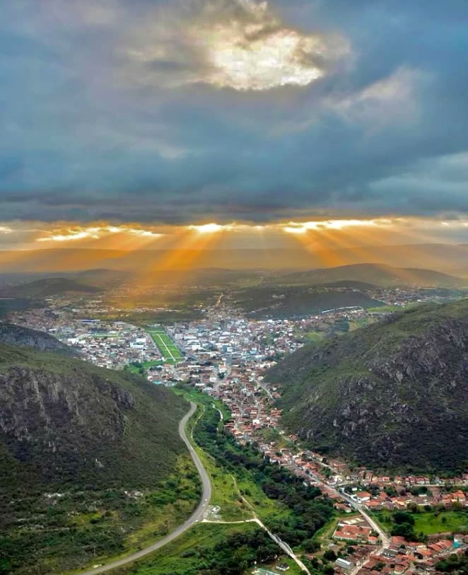 Vista aérea de Jacobina entre as serras, com o sol atravessando as nuvens no fim da tarde