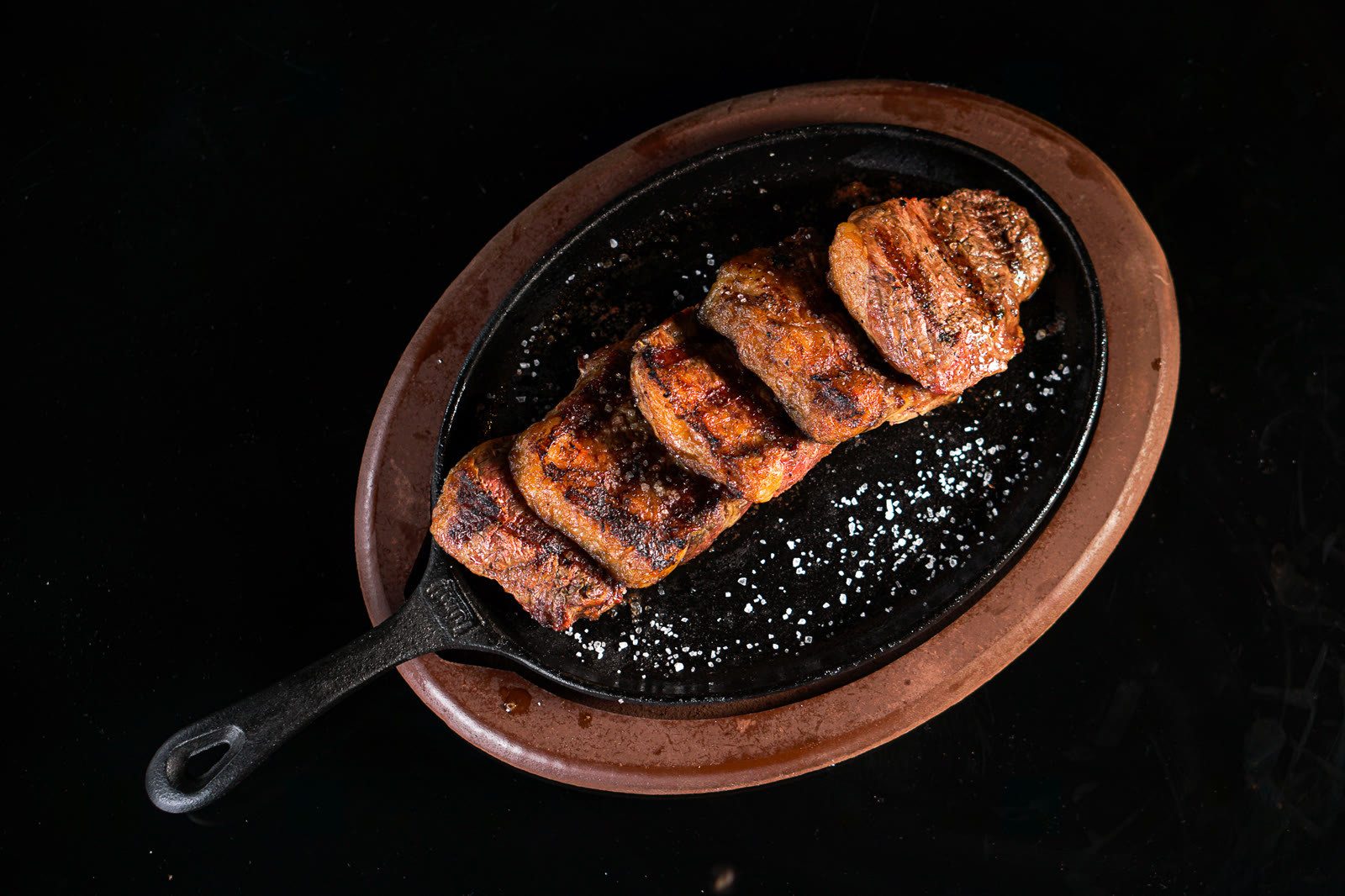 Picanha fatiada com crosta marcada e sal grosso, servida na chapa de ferro